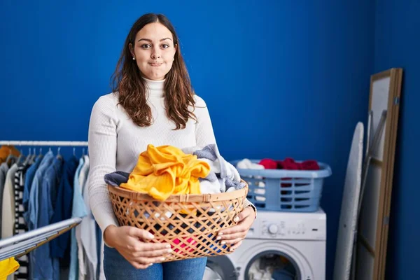 Young Hispanic Woman Holding Laundry Basket Puffing Cheeks Funny Face — Stock Photo, Image