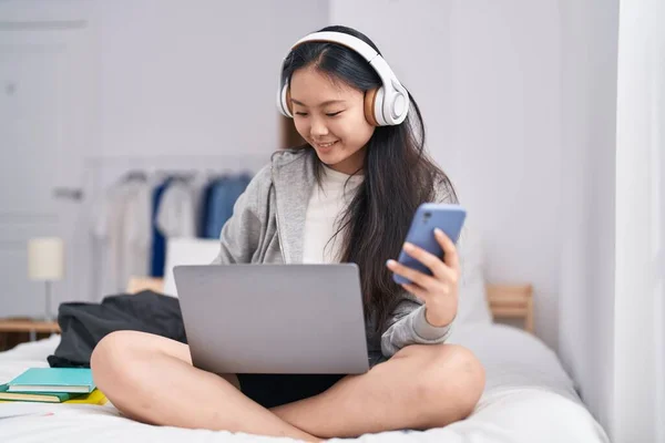 Young chinese woman listening to music using smartphone at bedroom