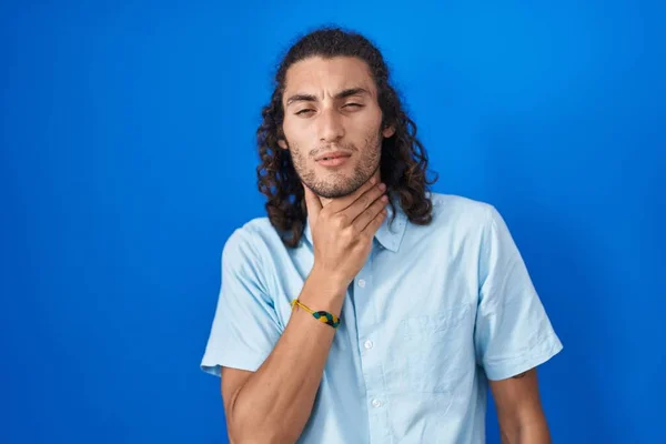 若いヒスパニック系の男は 痛みを伴う首に触れる青い背景の上に立って インフルエンザ 雲と感染症のための喉の痛み — ストック写真