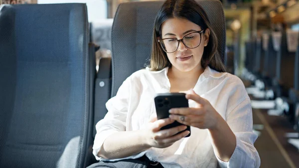 列車のワゴンの中に座っているスマートフォンを使用して微笑む若い美しいヒスパニックの女性 — ストック写真