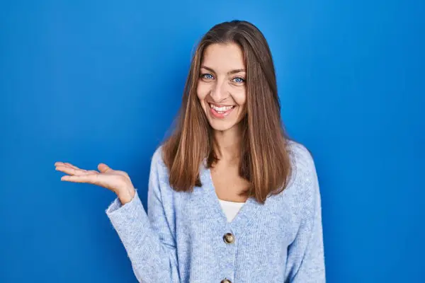 Young Woman Standing Blue Background Smiling Cheerful Presenting Pointing Palm — Zdjęcie stockowe