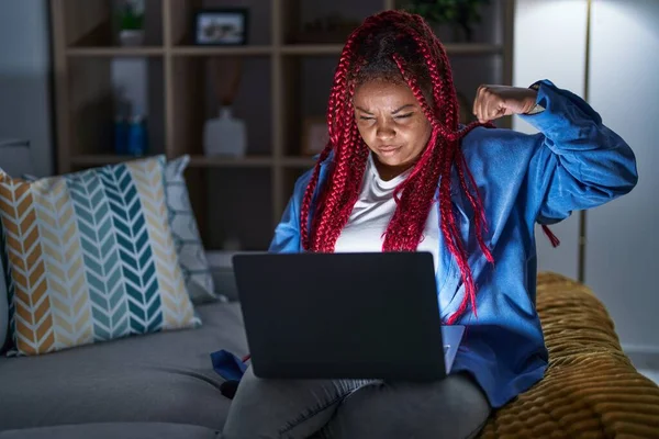 拥有辫子的非洲裔美国女人在夜间使用电脑笔记本电脑 强壮的男人表现出臂膀肌肉 自信而自豪 — 图库照片