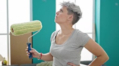 Yeni evinde elinde şüpheli bir ifadeyle boya silindiri tutan genç bir kadın.