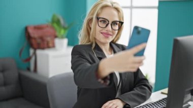 Genç sarışın iş kadını ofiste çalışan akıllı telefondan selfie çekiyor.