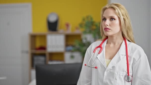 年轻的金发碧眼的女医生站在诊所里 严肃的表情和双臂交叉的姿势 — 图库视频影像