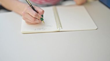 Masaya oturmuş, not defterine yazı yazan genç sarışın kadın kahve dükkanının terasında düşünüyor.