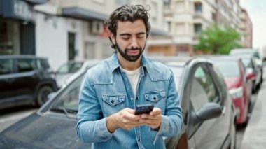 Genç İspanyol adam akıllı telefon kullanıyor. Arabasının yanında bekliyor.