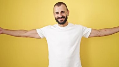 Genç İspanyol adam güçlü hareketler yapıyor. Kolları izole edilmiş sarı arka planda gülümsüyor.