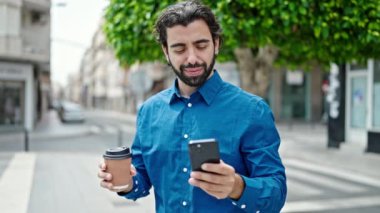Genç İspanyol adam akıllı telefon kullanıyor, sokakta kahve içiyor.