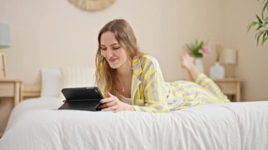 Yatak odasında dokunmatik ped kullanan genç sarışın kadın.