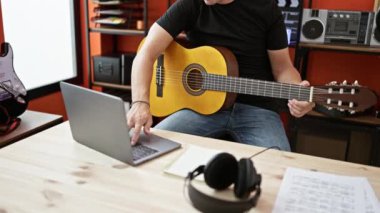Genç İspanyol müzisyen müzik stüdyosunda dizüstü bilgisayar kullanarak klasik gitar çalıyor.