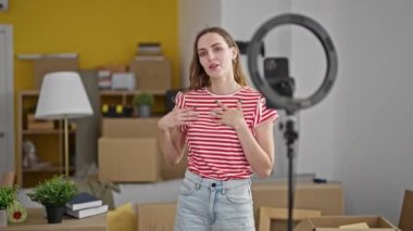 Genç sarışın kadın yeni evinde akıllı telefondan video dersi kaydediyor.