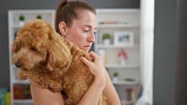 Genç, beyaz, köpekli bir kadın evde üzgün üzgün bakıyor.