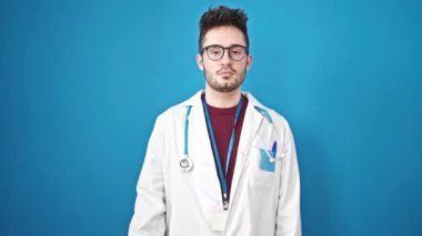 Genç İspanyol doktor gülümsüyor. Kendine güveni tam. Mavi arka planda şampuan şişesi tutuyor.