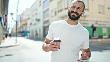 Latin kökenli genç adam kahve içiyor ve sokakta elini kolunu sallayarak arıyor.