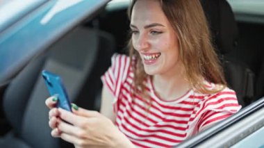 Genç sarışın kadın akıllı telefon kullanıyor. Sokakta arabada oturuyor.