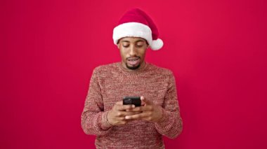 Afrika kökenli Amerikalı bir adam Noel şapkası takıyor. Akıllı telefon kullanıyor.