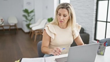 Genç sarışın iş kadını laptopla ofiste not alıyor.