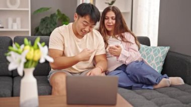 Kanepede oturan bir erkek ve bir kadın evde kahve içerken görüntülü konuşma yapıyorlar.