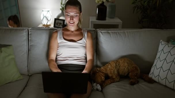 Молодая Белая Женщина Собакой Улыбается Используя Ноутбук Сидя Дома Диване — стоковое видео