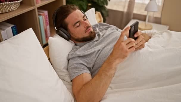 Joven Hombre Hispano Usando Smartphone Acostado Cama Usando Auriculares Dormitorio — Vídeos de Stock