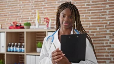 Afro-Amerikan kadın doktor elinde bir dosya, klinikte gülümsüyor.