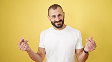 Young hispanic man smiling confident doing spend money gesture over isolated yellow background