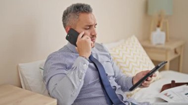 Genç İspanyol iş adamı otel odasında dokunmatik ped kullanarak akıllı telefondan konuşuyor.