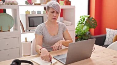 Yemek odasında dizüstü bilgisayar kullanan genç bir kadın.