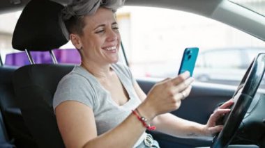 Sokakta arabada oturan akıllı telefonu kullanan genç bir kadın.