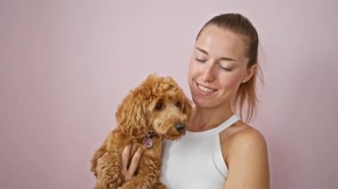 Köpeği olan beyaz bir kadın pembe arka planda öpüşürken gülümsüyor.