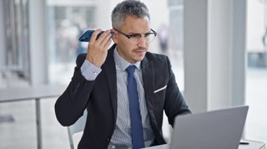 Genç İspanyol iş adamı ofisteki bilgisayarla akıllı telefondan sesli mesaj dinliyor.