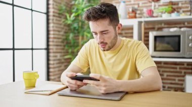 İspanyol asıllı genç bir adam yemek odasında masada oturmuş video oyunu oynuyor.