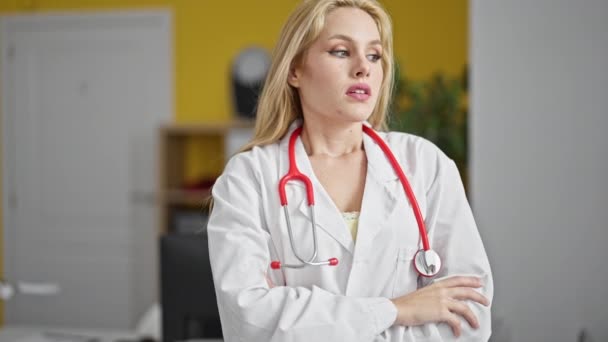 若い金髪の女性医師は クリニックで考えている疑わしい表現で立っています — ストック動画