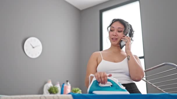 年轻美丽的惊慌失措的女人用智能手机在洗衣房用熨衣机烫衣服 — 图库视频影像