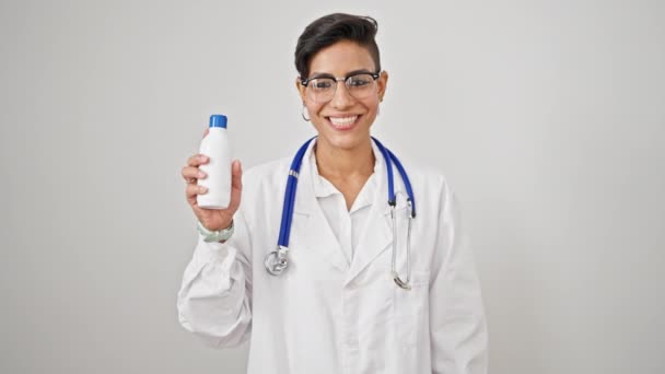 若い美しいヒスパニックの女性医師は 孤立した白い背景の上に薬瓶を保持する自信を持って微笑みます — ストック動画