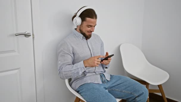 Jovem Hispânico Usando Smartphone Fones Ouvido Sentados Cadeira Sorrindo Sala — Vídeo de Stock