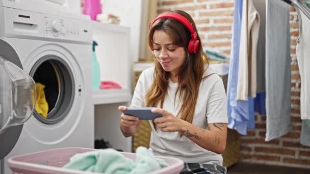 年轻美丽的惊慌失措的女人在洗衣房里玩电子游戏洗衣服 — 图库视频影像