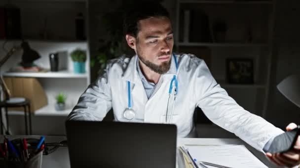 Jovem Hispânico Homem Médico Usando Laptop Falando Por Telefone Clínica — Vídeo de Stock