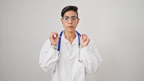 若い美しいヒスパニックの女性医師は 孤立した白い背景の上に落ち着いたジェスチャーをしている深刻な表情で立っています — ストック動画