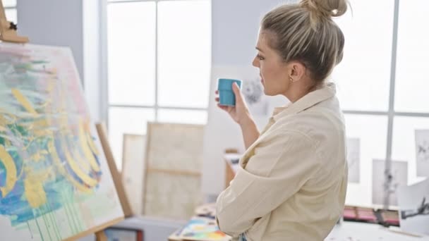 年轻的金发碧眼的女艺术家在艺术工作室里拉着一杯咖啡 — 图库视频影像