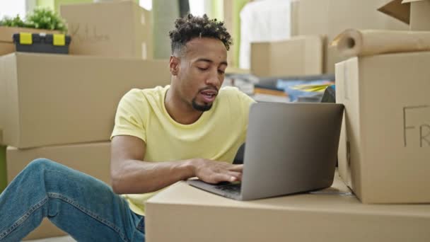 アフリカ系アメリカ人男性が床に座ってノートパソコンを使い 新しい家でアイデアを持っています — ストック動画