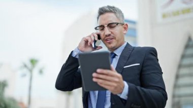Latin kökenli genç bir iş adamı akıllı telefondan konuşuyor. Sokakta dokunmatik ped kullanıyor.