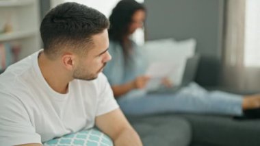 Erkek ve kadın çift kanepede otururken kız arkadaşları evde çalışırken üzgün görünüyorlar.