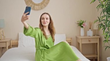Genç sarışın kadın yatakta akıllı telefonuyla selfie çekiyor.