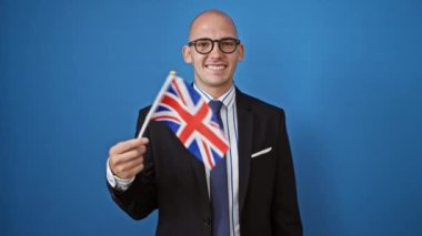 Genç İspanyol işçi Birleşik Krallık bayrağını tutuyor ve mavi arka planda gülümsüyor.