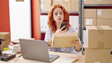 Genç kızıl saçlı kadın ecommerce iş işçisi. Ofiste akıllı telefon kullanarak paketleri tarıyor.