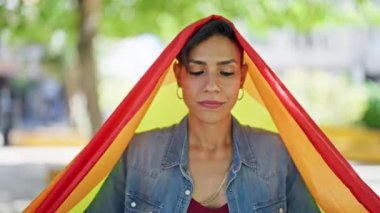 Parkta gökkuşağı bayrağı tutan güzel İspanyol kadın gülümsüyor.
