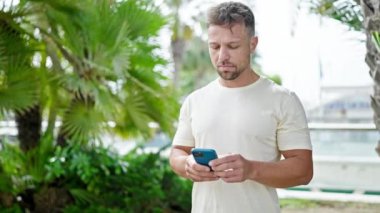 Parkta gülümseyen akıllı telefon kullanan genç adam.