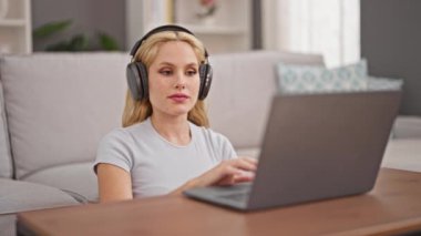 Genç sarışın kadın evde oturmuş müzik dinliyor ve dans ediyor.